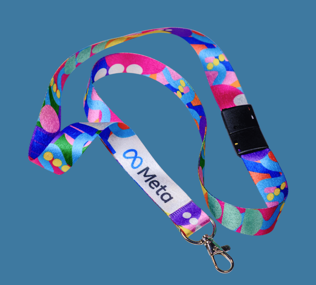 Colourful patterned fabric lanyard with a white “Meta” logo section, black safety breakaway clip and silver swivel hook, shown coiled on a solid blue background.
